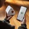 Person holding the Goodnature Mouse Trap in one hand and a smartphone in the other, app open on screen.